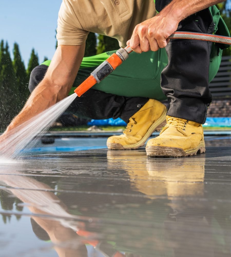 Caucasian Men Washing His Swimming Pool Composite Made Deck Using Water Hose. Backyard Maintenance Job.